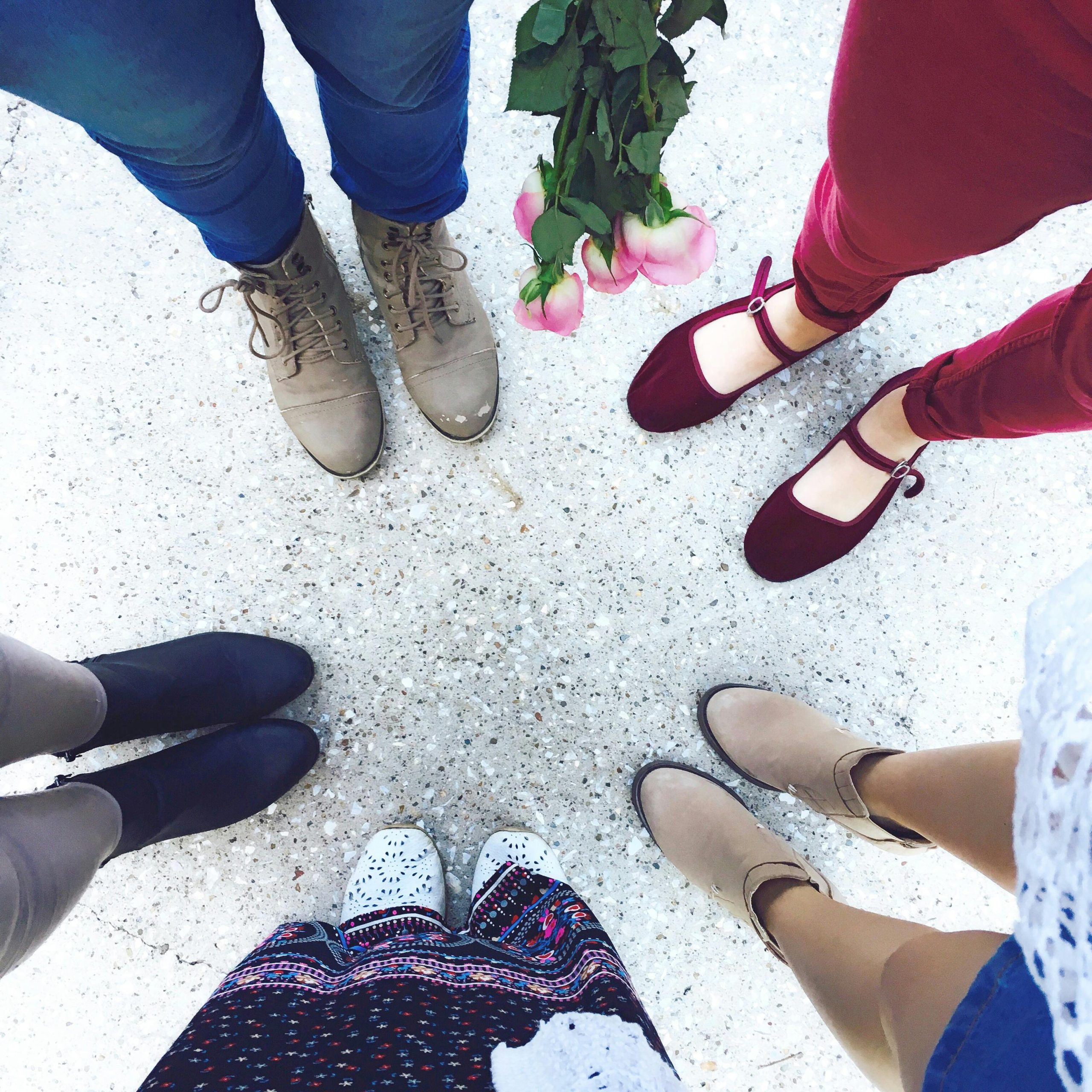 Top view of women in stylish shoes forming a circle outdoors holding pink roses.